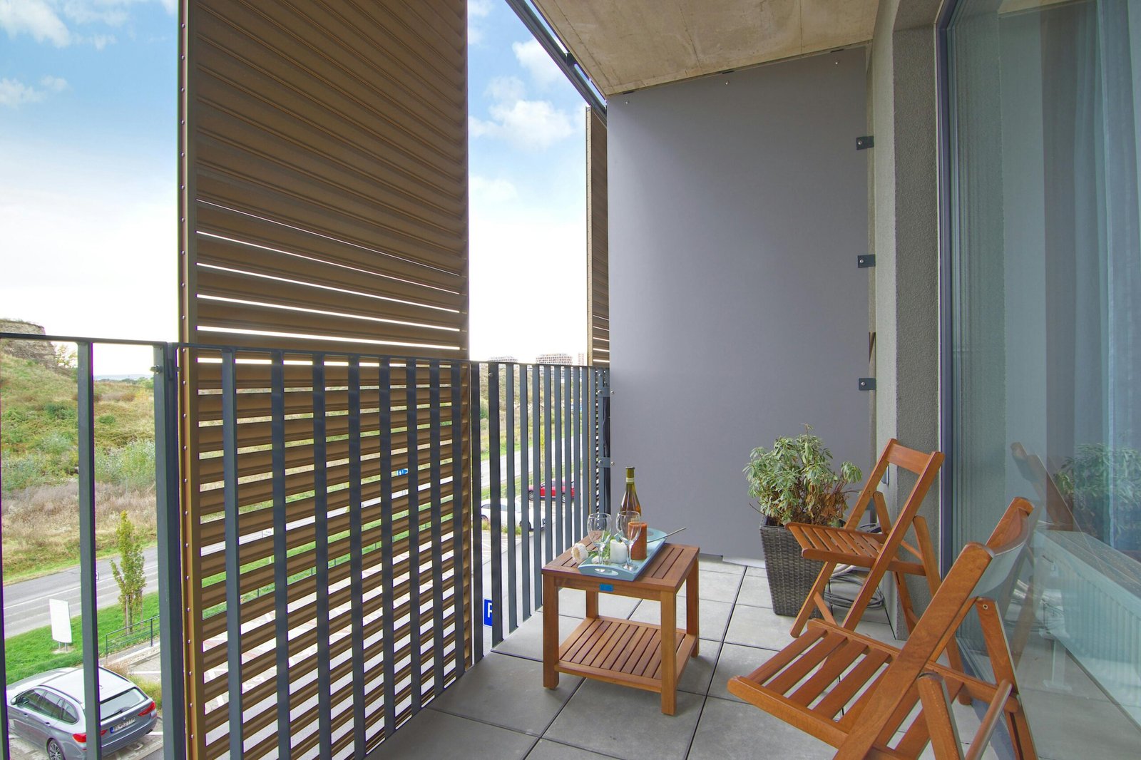 A contemporary balcony featuring wooden chairs, table, and glass wall with a view.
